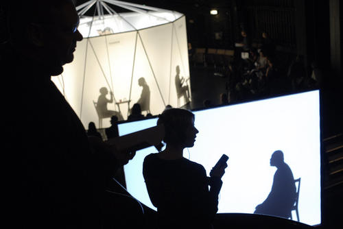 Blick in den dunklen Theatersaal: Im Zuschauerraum läuft der Silhouettenfilm, auf der Drehbühne kreist das Expertenkarussell zum ersten Mal. Die Schatten gehören der Choreographin Sasha Waltz und die Philosophin Catherine Newmark.